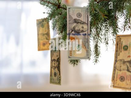 Various US Dollar bills hanging on a Christmas tree as ornaments with a bright, light background. A Christmas cost concept. Stock Photo