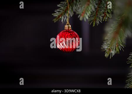 A  closeup of a red Christmas bauble hanging on a Christmas tree with a dark background. A Christmas elements background. Stock Photo