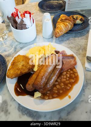 Full English breakfast being eaten by business traveller in a Belfast hotel, Northern Ireland, with scrambled egg, sausages, bacon, beans, hash browns Stock Photo