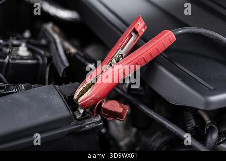 Car battery charging with jumper cables in vehicle engine bay during emergency power boost Stock Photo
