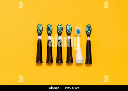 Five black new toothbrushes and one old white toothbrush on a yellow background Stock Photo