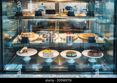Assorted cakes, pies and desserts on plates and wooden trays inside glass refrigerated showcase in bakery or cafe shop Stock Photo