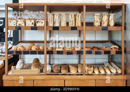 Variety of fresh baked sourdough, seeded bread, croissants, danishes, and baguettes display on wooden shelf in bakery shop Stock Photo