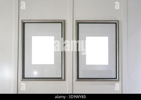 Two mettallic picture frames with blank white center mounted on clean grey panel, mockup interior design presentation Stock Photo