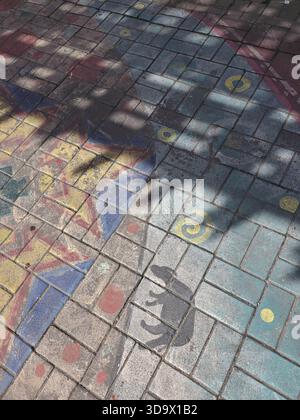 Colorful patterned pavement displays an abstract design, beautifully illuminated by dappled sunlight. Tree shadows create vibrant, playful effect grou Stock Photo