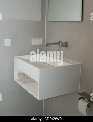 Minimalist bathroom scene featuring a floating white vanity, built-in towel shelf, soft neutral tiles, and a wall-mounted faucet. Clean architecture Stock Photo