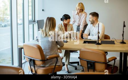 Five professionals engage in a meeting at a contemporary office. They are discussing ideas while using a tablet and sharing insights in a collaborativ Stock Photo