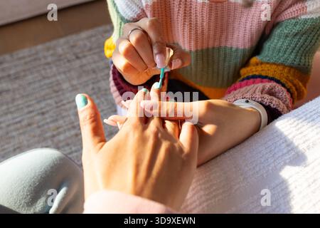 Turquoise nail polish being applied with small brush over white towel on padded armrest in sunlight Stock Photo