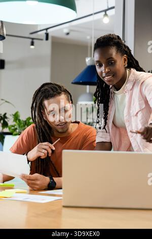 African American colleagues leaning and pointing at laptop while reviewing papers in modern office Stock Photo