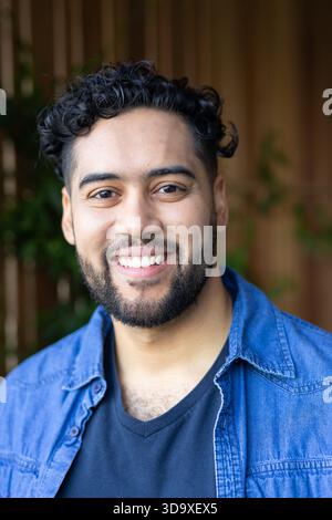 Man smiling and looking at camera on covered patio wearing denim shirt and black v-neck t-shirt Stock Photo