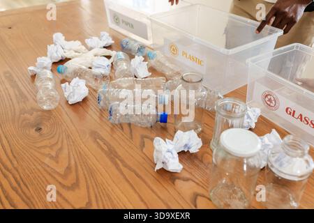 Empty plastic bottles and crumpled paper are being sorted into labeled bins on wooden table Stock Photo