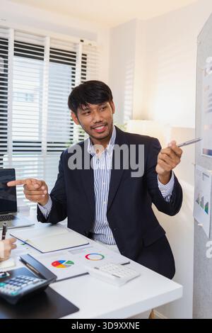 Business colleagues are engaged in a collaborative discussion, analyzing financial charts and reports on the wall and table. They exchange ideas, revi Stock Photo