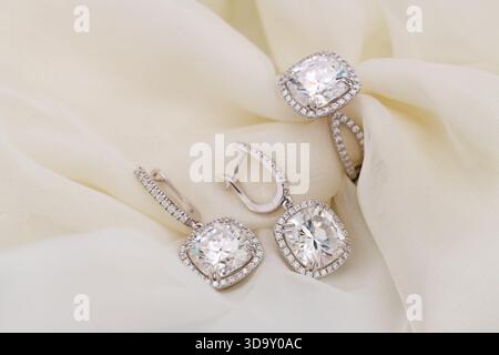 A set of diamond earrings and a diamond ring are displayed on a white cloth. The earrings are large and diamond-encrusted, while the ring is smaller a Stock Photo