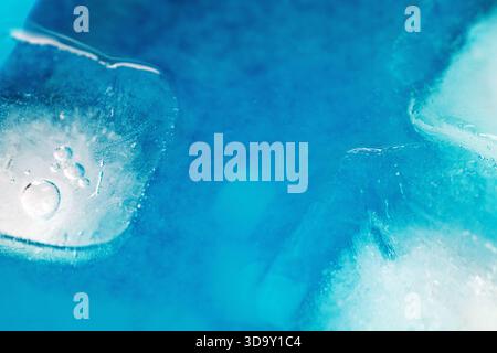 A blue and white background with ice cubes in the foreground. The ice cubes are melting and the water is blue Stock Photo