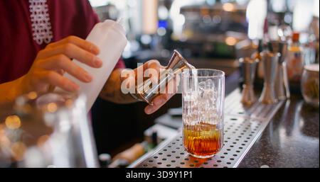 Cocktail recipe. Making beverage mix. Bartender pouring sweet aroma color syrup from metal jigger to glass. Flavored refreshing drink. Stock Photo