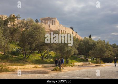 Athens, Greece - March 20, 2025: The Parthenon atop the Acropolis stands bathed in golden light against dramatic clouds, surrounded by olive trees and Stock Photo
