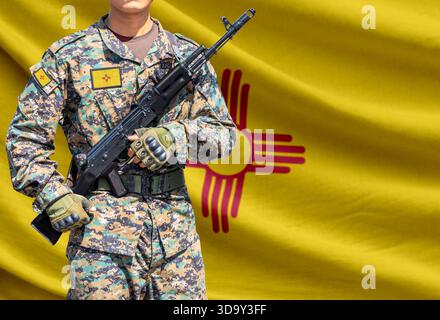 New Mexico US state flag with soldier in military uniform holding assault rifle in front of it Stock Photo