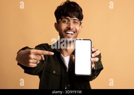 Young Man Smiles and Points at His Smartphone Against a Warm Background Stock Photo