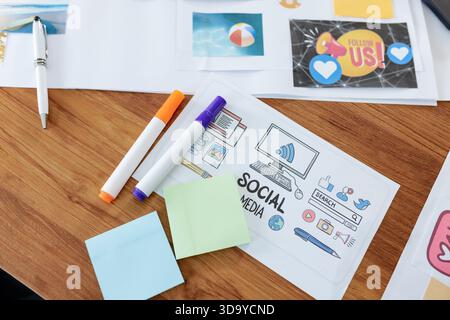 Sheet featuring SOCIAL MEDIA icons is sitting on wooden desk with markers and sticky notes nearby Stock Photo