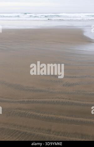 Rippled pattern in sand on a beach, with waves in background. Stock Photo