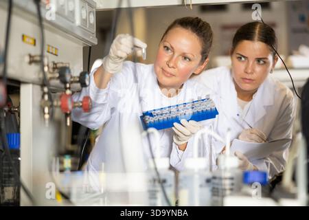 Female pharmacist researchers waiting for color change in test tubes while conducting experiments and making notes in laboratory Stock Photo