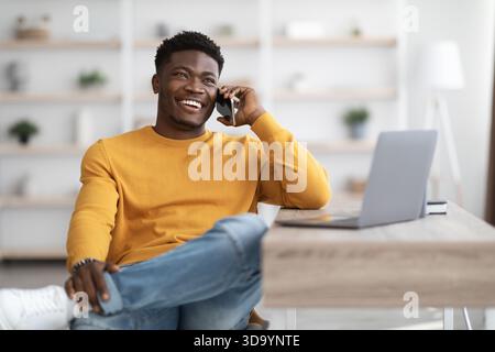 Cheerful man sitting at table with laptop, talking on phone Stock Photo