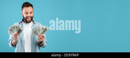 Excitement and Joy Displayed by a Man Holding Cash Against a Blue Background Stock Photo