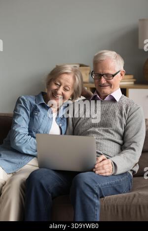 Happy mature spouses resting on sofa at home using laptop Stock Photo