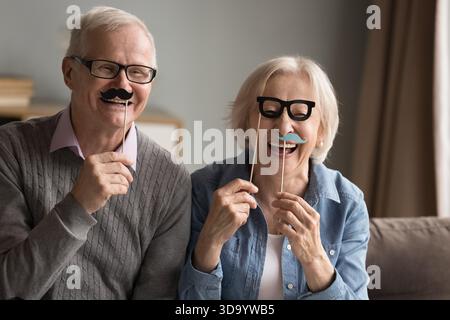Senior couple using moustache glasses on sticks for joyful portrait Stock Photo
