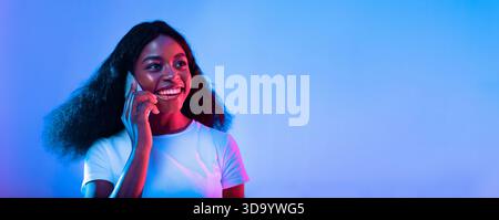 Young Woman Smiling While Talking on the Phone in Vibrant Lighting Stock Photo