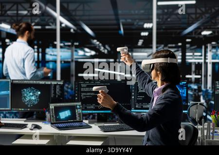 Data center programmer wearing VR goggles managing AI training datasets. IT worker using virtual reality tech, overseeing neural networks in server room supporting scalable equipment for AI apps Stock Photo