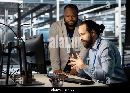 Technicians in data center office using computer, verifying firewall configurations. Teamworking IT specialists performing equipment vulnerability scans in server hub using PC Stock Photo