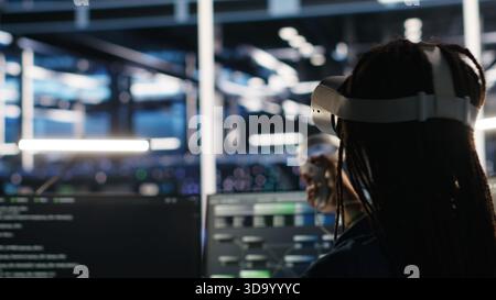 Server farm admin using VR equipment and node tree systems to categorize unstructured data. Data center IT specialist uses virtual reality headset and visual programming software, camera B Stock Photo