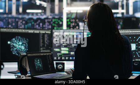 Data center programmer entering office uses node tree program to identify equipment performance issues. Server hub worker sitting at desk, reviewing data analysis graph to minimize failures, camera B Stock Photo