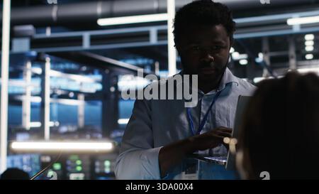 Server farm manager supervising engineer using node tree systems to categorize unstructured data. Data center supervisor overseeing IT expert using natural language processing software, camera B Stock Photo