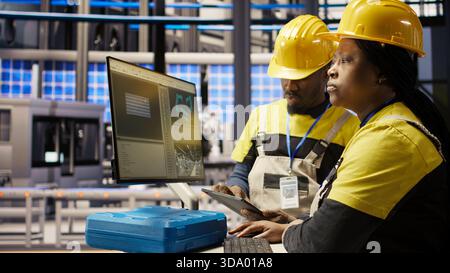 Smart factory manager overseeing work done by engineer calibrating high tech machinery and analyzing sensor data. Team leader supervising engineer troubleshooting assembly equipment, camera A Stock Photo
