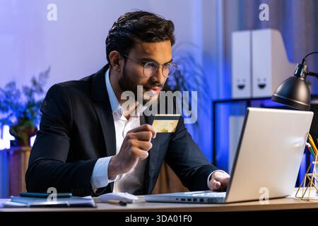 Arabian businessman programmer software developer working making online purchase payment shopping with credit bank card and use laptop at home office desk with laptop. Indian freelancer business man Stock Photo