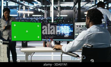 Data center worker with paraplegia using green screen PC to apply node tree programming. Server hub admin with disability uses visual programming on mockup computer to identify data patterns, camera B Stock Photo