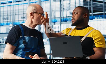Photovoltaics smart factory team leader teaching intern how to fix damaged IoT sensors using laptop. Industry 4.0 solar panels plant experienced engineer guiding trainee in reducing downtime, camera A Stock Photo