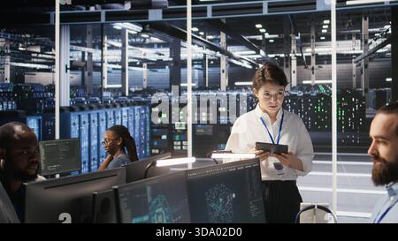 Server hub supervisor overseeing data scientist examining neural network algorithm on screen. Manager reviewing performance dashboards in artificial intelligence infrastructure environment, camera A Stock Photo