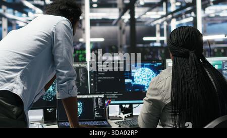 Data center manager supervising worker deploying AI solutions optimizing equipment. Server farm supervisor overseeing programmer using artificial intelligence to minimize systems downtime, camera B Stock Photo
