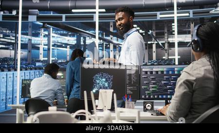 Happy data center admin uses node tree programming on laptop to identify equipment performance issues. Cheerful server farm worker reviews data analysis graph to minimize hardware failures, camera A Stock Photo