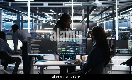 Data center manager supervising technician using node tree software to analyze datasets. Server room team leader oversees IT expert using visual programming tools to improve gear performance, camera A Stock Photo