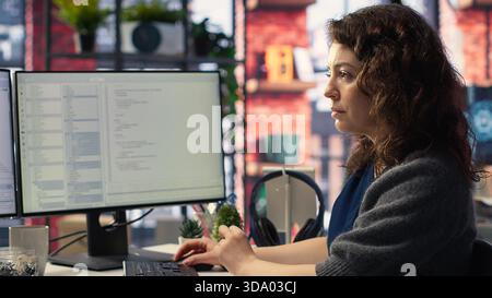 Female programmer developing app and software algorithm on pc, working at creative agency. Engineer uses digital tools and focuses on java script engineering and coding, IT specialist. Camera B. Stock Photo