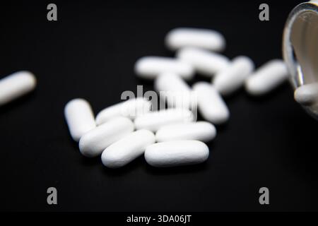 White prescription pills scattered on a black background, creating a clean medical, pharmaceutical, and healthcare-themed image. Stock Photo