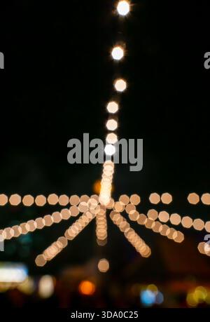 Out-of-focus string lights at a fair or Christmas market, captured in vertical orientation with a strong bokeh effect. Stock Photo