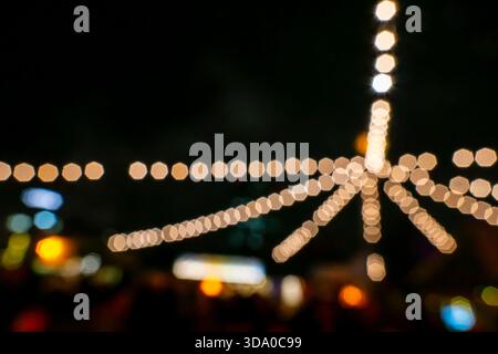 Out-of-focus string lights at a fair or Christmas market, captured in horizontal orientation with a strong bokeh effect. Stock Photo