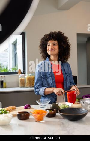 African American woman chopping red bell pepper in kitchen on marble countertop with chef's knife Stock Photo