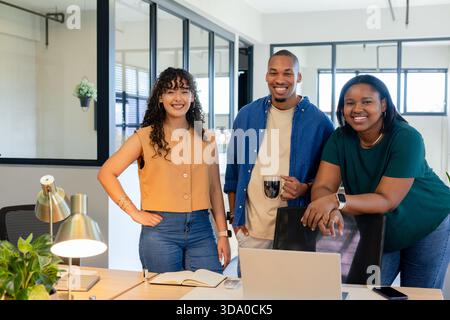 Diverse coworkers in business attire collaborating around laptop at office desk with coffee mug Stock Photo