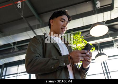 Asian man holding smartphone reading screen in office with leather bracelets, plant, pendant lamps Stock Photo